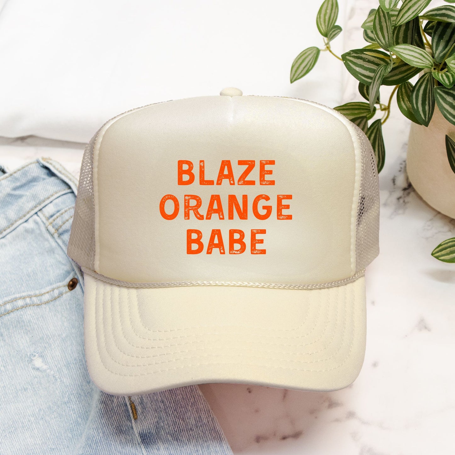 Beige cap with 'BLAZE ORANGE BABE' text on a blurred background