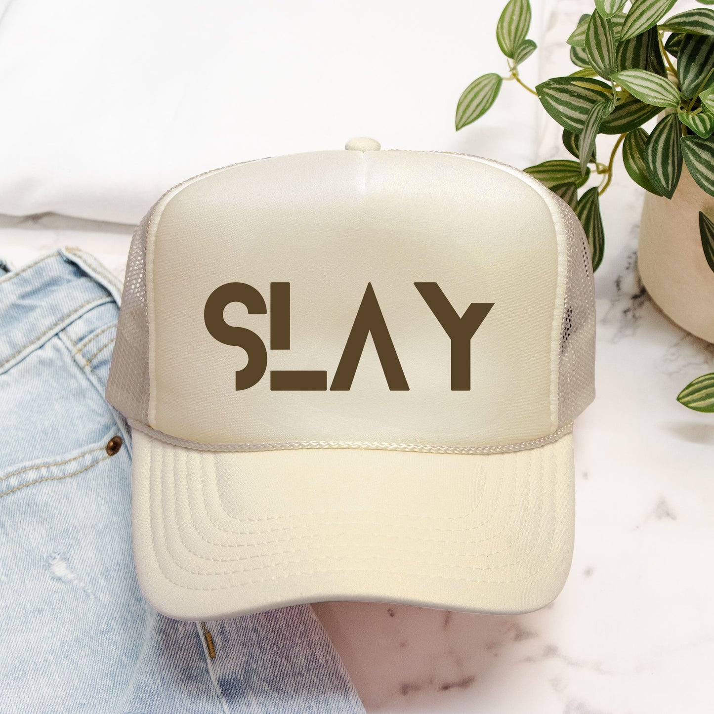 Beige trucker hat with 'SLAY' text on a blurred background