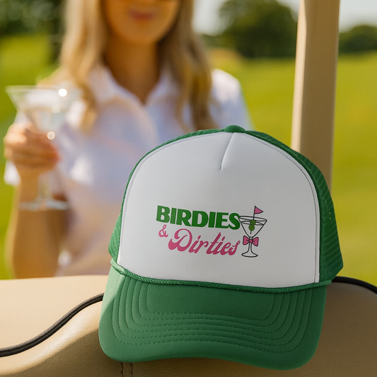 Green and white cap with 'Birdies & Dirties' text on a golf cart, woman holding a drink in the background.