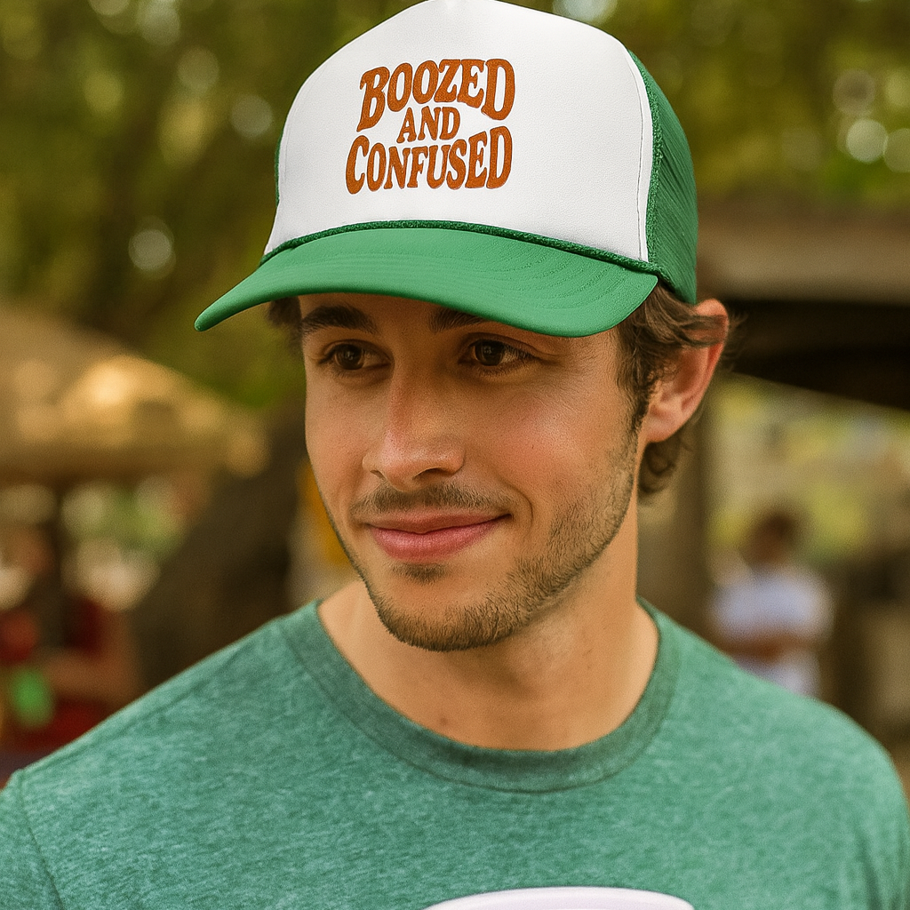 Man wearing a cap with 'Boozed and Confused' text, holding a red cup outdoors.