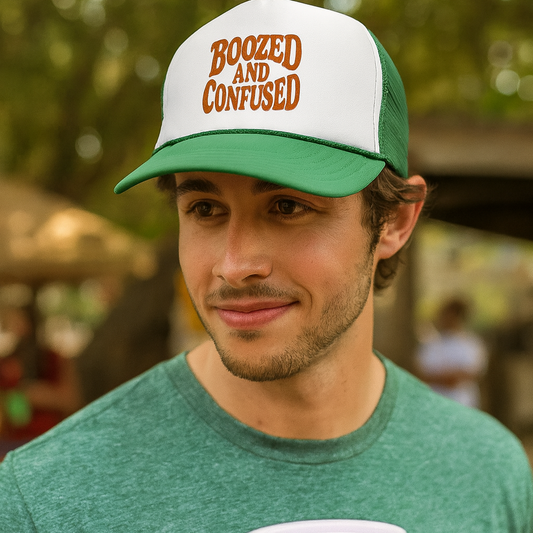 Man wearing a cap with 'Boozed and Confused' text, holding a red cup outdoors.