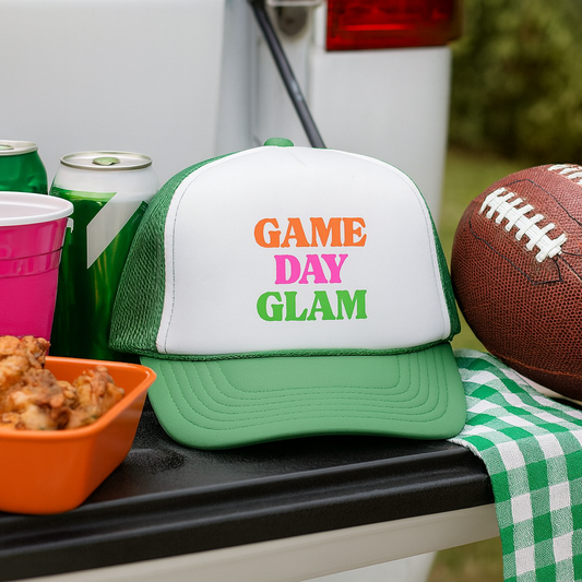 Green and white cap with 'Game Day Glam' text on a tailgate with snacks and a football.