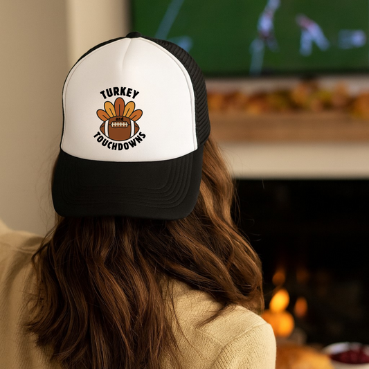 Person wearing a cap with 'Turkey Touchdowns' design in front of a TV screen.