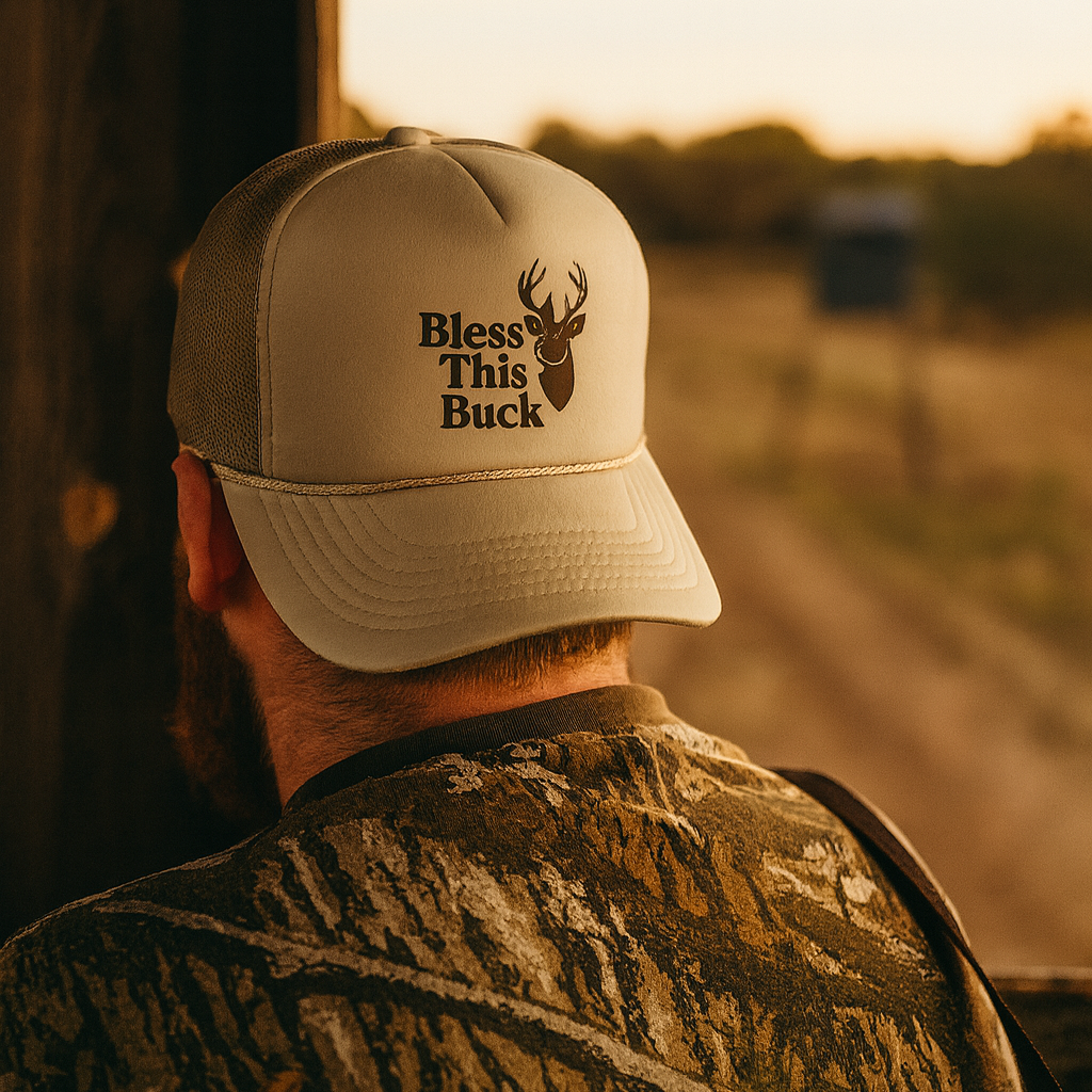 Man wearing a cap with 'Bless This Buck' text and a deer graphic, standing on a dirt road at sunset.