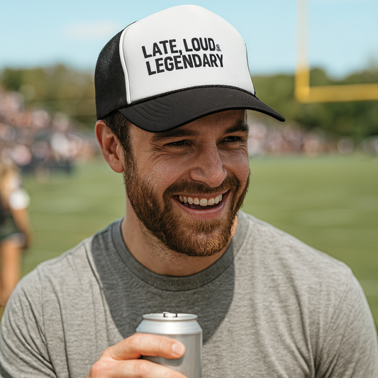 Man wearing a cap with 'LATE, LOUD & LEGENDARY' text, holding a can on a sports field.