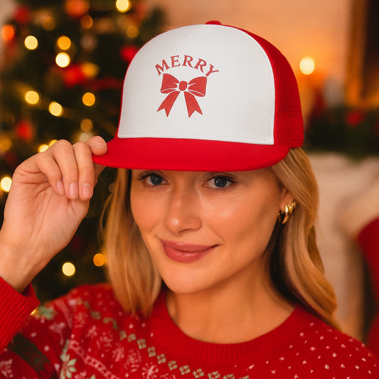 Person wearing a red and white Christmas-themed cap with 'Merry' and a bow design, standing in front of a decorated Christmas tree.