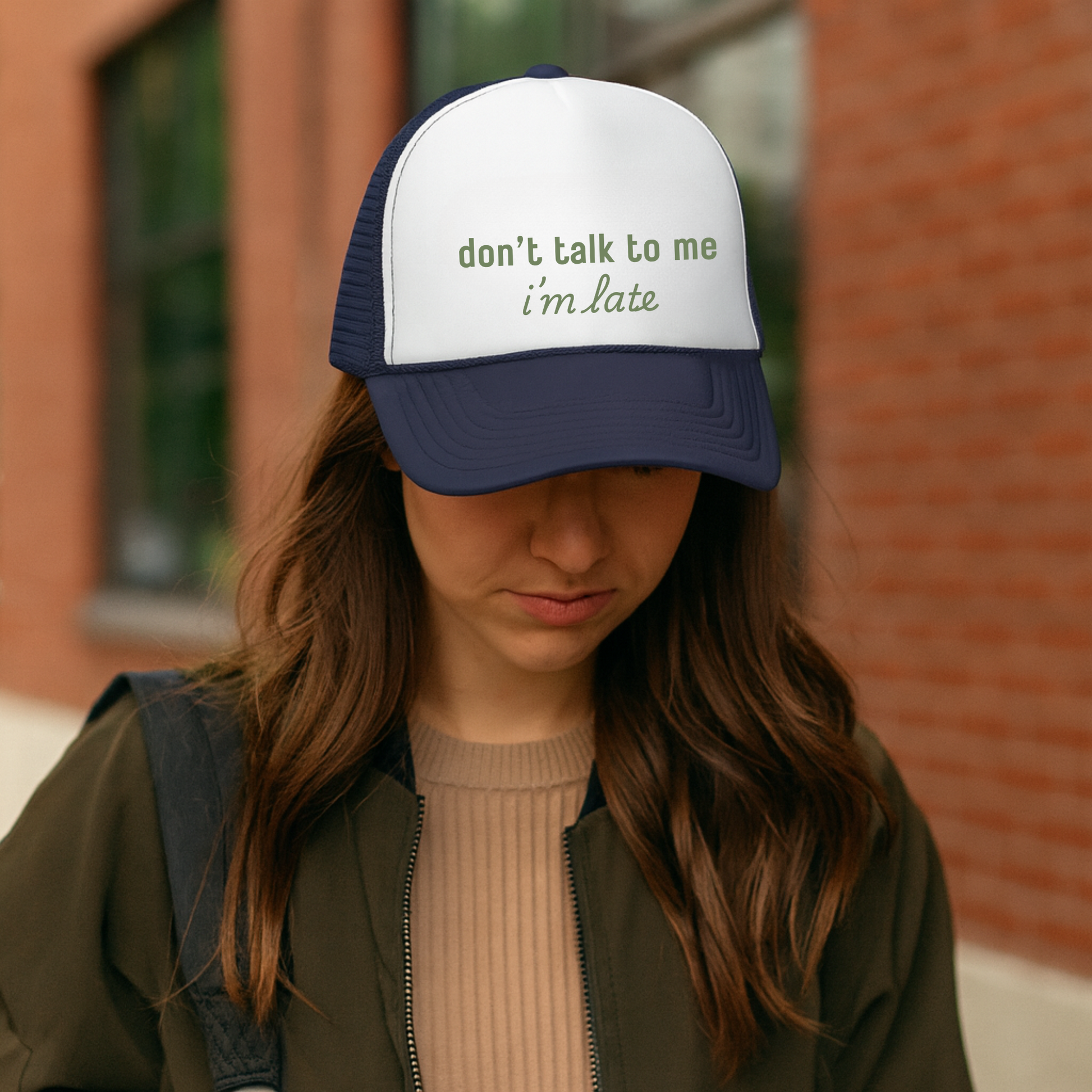Person wearing a cap with 'don't talk to me i'm late' text in front of a brick wall.
