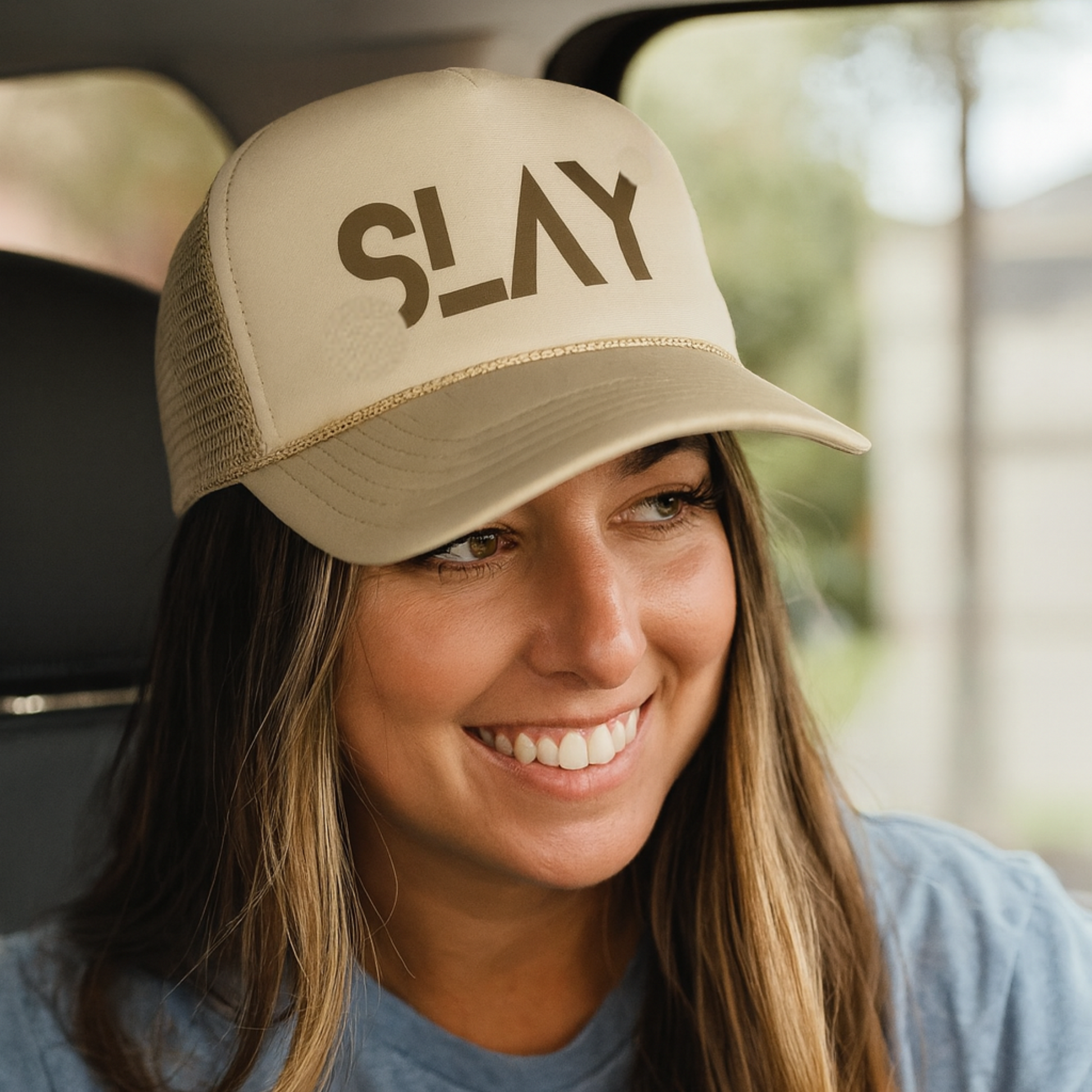 girl wearing a tan trucker hat that says SLAY in fun trendy brown font