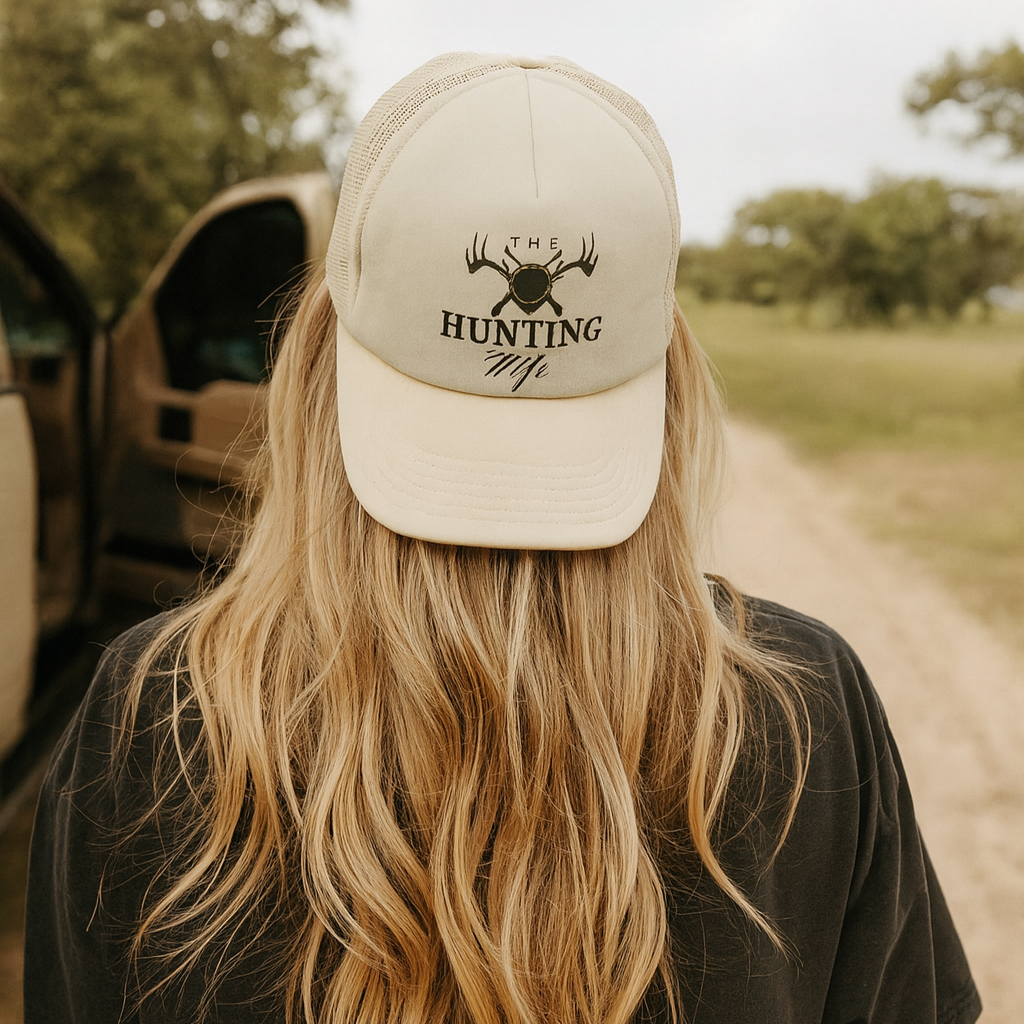 Person wearing a cap with 'Hunting Wife' text and logo on a dirt road.