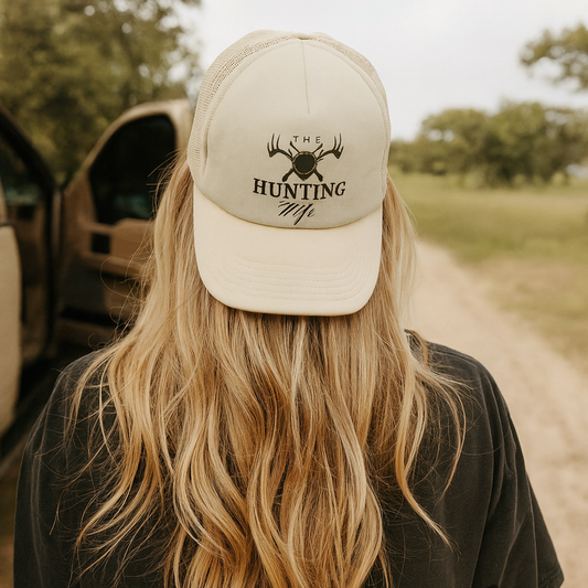 Person wearing a cap with 'Hunting Wife' text and logo on a dirt road.